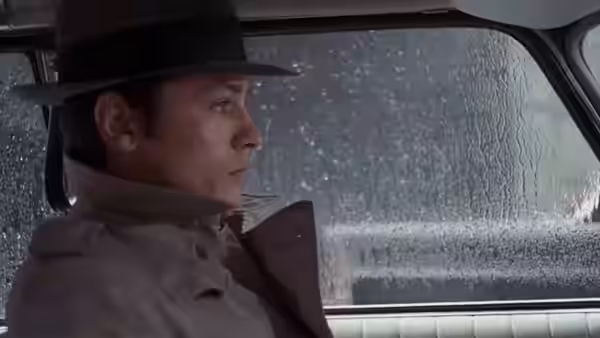 Jef Costello (Alain Delon) sits in a car beside a rain-streaked window