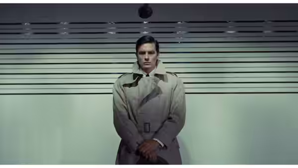 Jef Costello (Alain Delon) stands alone before horizontal blinds, hands clasped