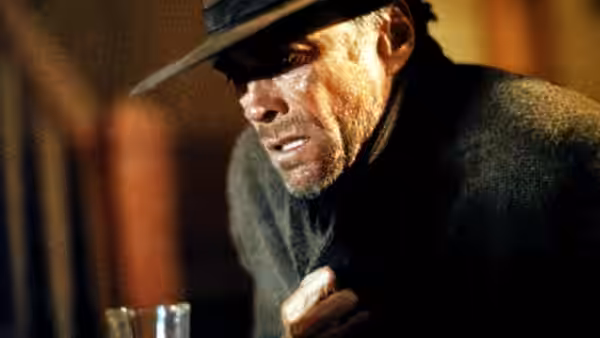 William Munny (Clint Eastwood) crouching with a clenched fist and gritted teeth