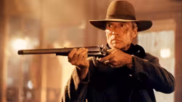William Munny (Clint Eastwood) aiming a shotgun while standing indoors