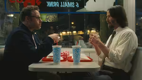 Aziz Ansari and Seth Rogen eating burgers across from each other in a diner booth