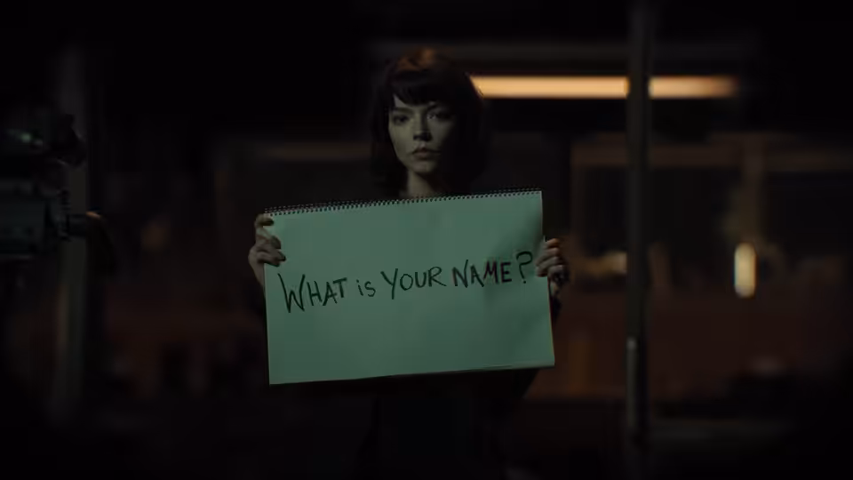 Drasa (Anya Taylor-Joy) holding a notepad reading what is your name