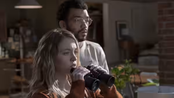 Pippa (Sydney Sweeney) peering through binoculars with Thomas (Justice Smith) behind