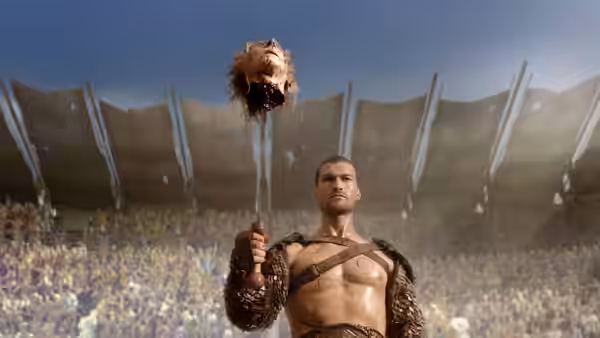 Spartacus (Andy Whitfield) raises a severed head before a cheering arena crowd
