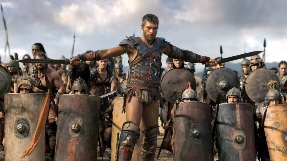 Spartacus (Andy Whitfield) stands with arms outstretched among his armed warriors