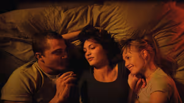 Murphy (Karl Glusman) lying in bed between Electra (Aomi Muyock) and Omi (Klara Kristin)