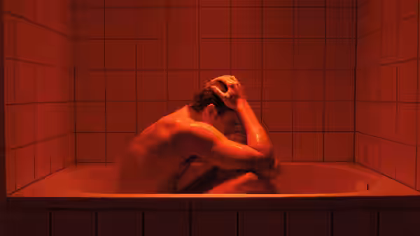 Murphy (Karl Glusman) hunched in a red-lit bathtub with head in hands