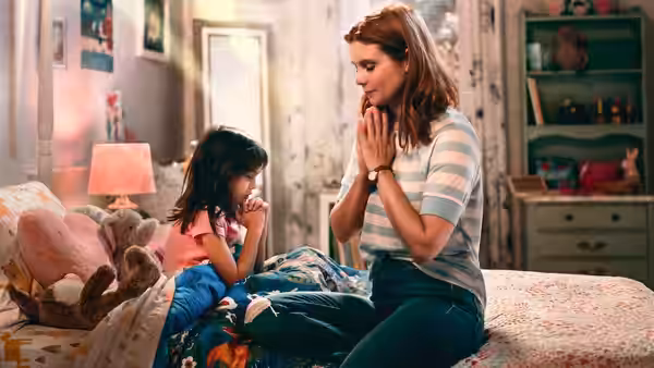 Maddie Townsend (Joanna Garcia) praying with a young girl on a bedroom bed