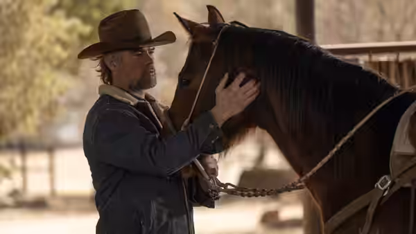 Man in brown hat gently touching head of dark brown horse