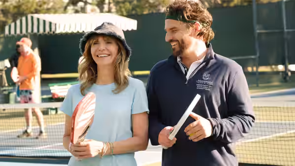 Mary Steenburgen holding a paddle beside Jake Johnson on a tennis court