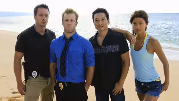Two men with police badges stand on the beach with a man and woman
