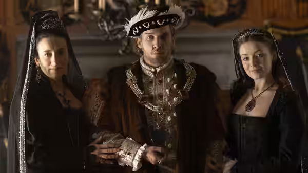 Henry VIII (Jonathan Rhys Meyers) stands between two women in black gowns