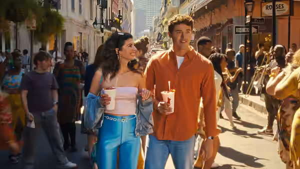 Poppy (Emily Bader) and Alex (Tom Blyth) walking a busy sidewalk holding drinks