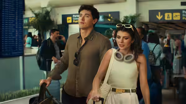 Alex (Tom Blyth) and Poppy (Emily Bader) walking through a crowded airport terminal