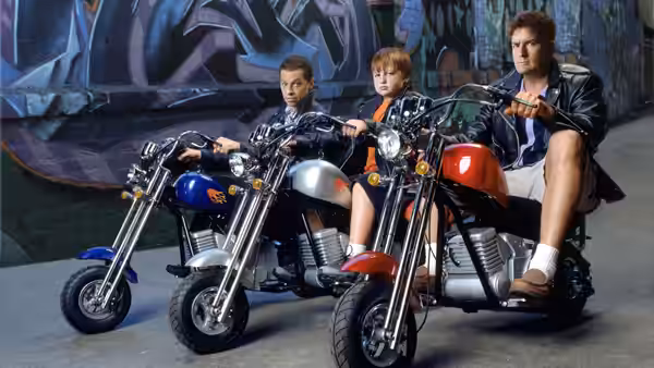 Charlie Harper with two boys sitting on motorcycles before a graffiti wall
