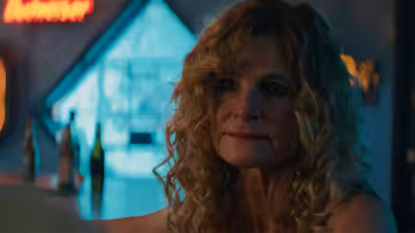 Deborah (Kyra Sedgwick) sits at a dimly lit bar counter with a serious expression