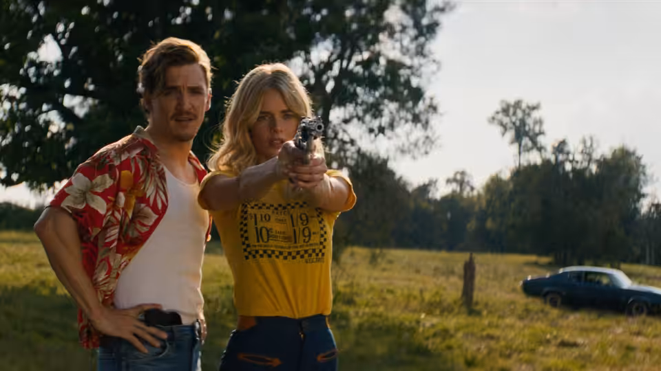 Caroline Daniels (Samara Weaving) aims a revolver while Oliver Anderson (Kyle Gallner) stands beside her in a field