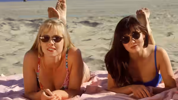 Two women lying on towels on the sand with feet raised