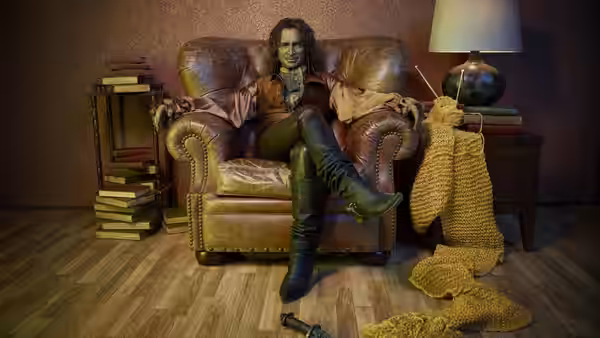 Rumplestiltskin (Robert Carlyle) lounging in a leather armchair with knitting