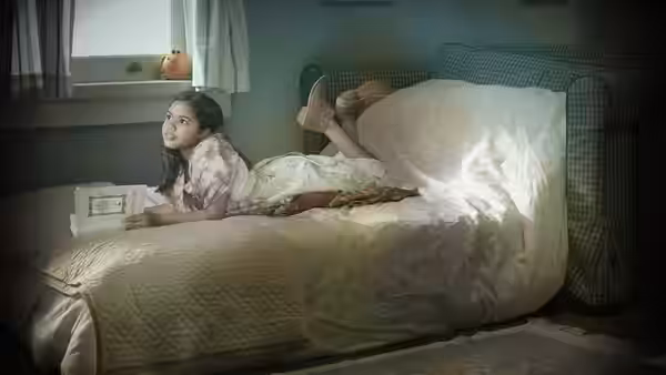 A young girl lying on a bed reading an open book