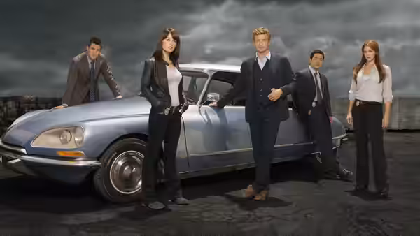 Patrick Jane (Simon Baker) and team gather around a vintage blue car