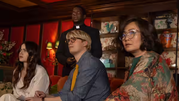Elliot Matthews (Nicholas Galitzine) sits between two women in a room