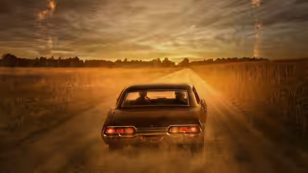 a black car driving down a rural road at sunset kicking up dust