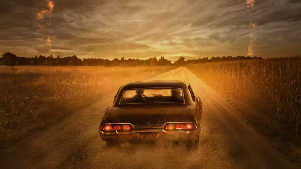 a black car driving down a rural road at sunset kicking up dust