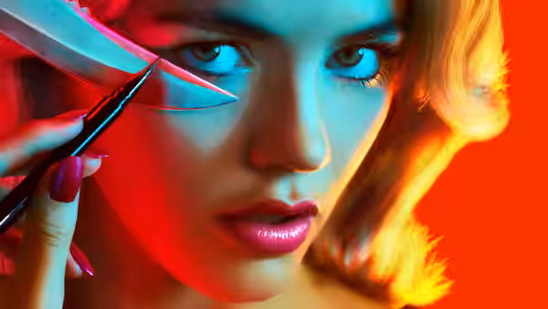 Woman with pink hair applying eyeliner using a knife against a red backdrop