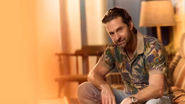 R.J. Decker (Scott Speedman) sits on a couch in a living room