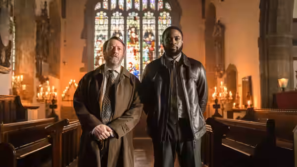 John Taylor (David Mitchell) and DI Russell Carter (Dipo Ola) standing in a church