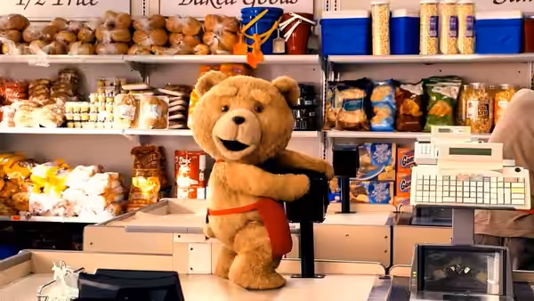 Ted stands behind a bakery counter wearing a red apron