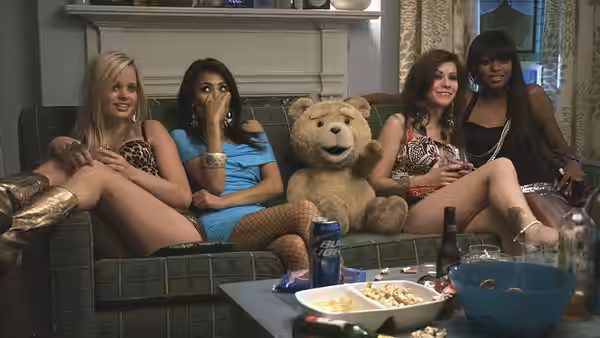 Women lounge with Ted on a living-room couch amid drinks and party snacks