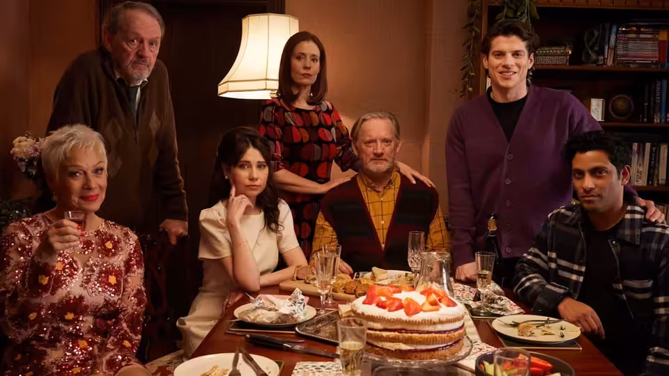 Seven relatives of various ages gathered around a dining table with a strawberry cake