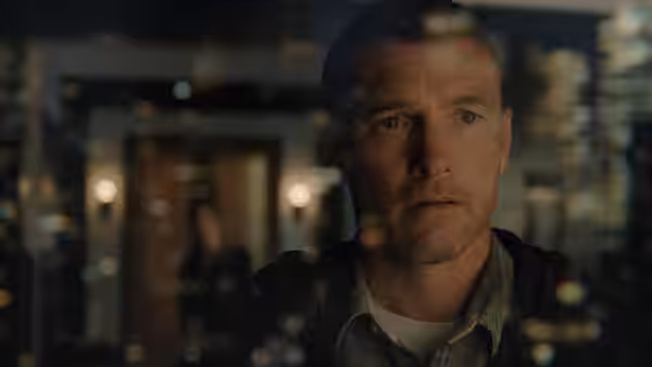 Man with short hair and stubble looking ahead against blurred nighttime lights