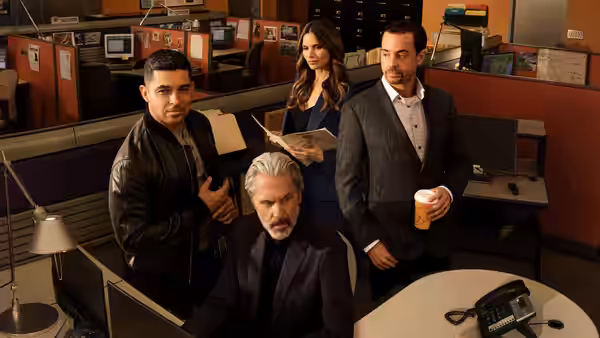Leroy Jethro Gibbs (Mark Harmon) seated at a desk with colleagues
