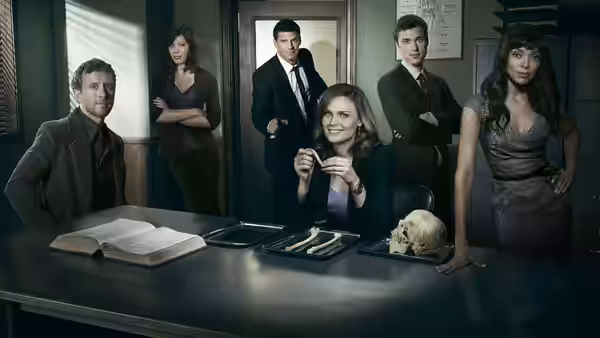 Brennan (Emily Deschanel) and colleagues gather around a table with a skull