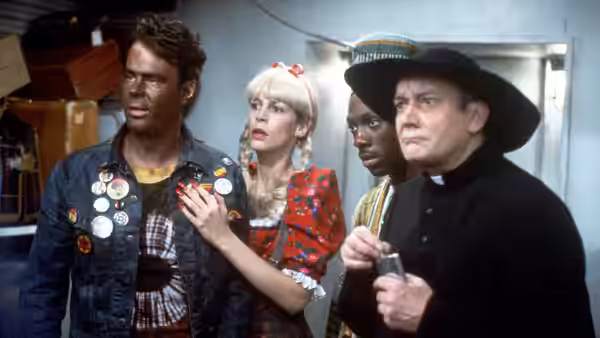 Four people standing together in a cluttered indoor space looking concerned