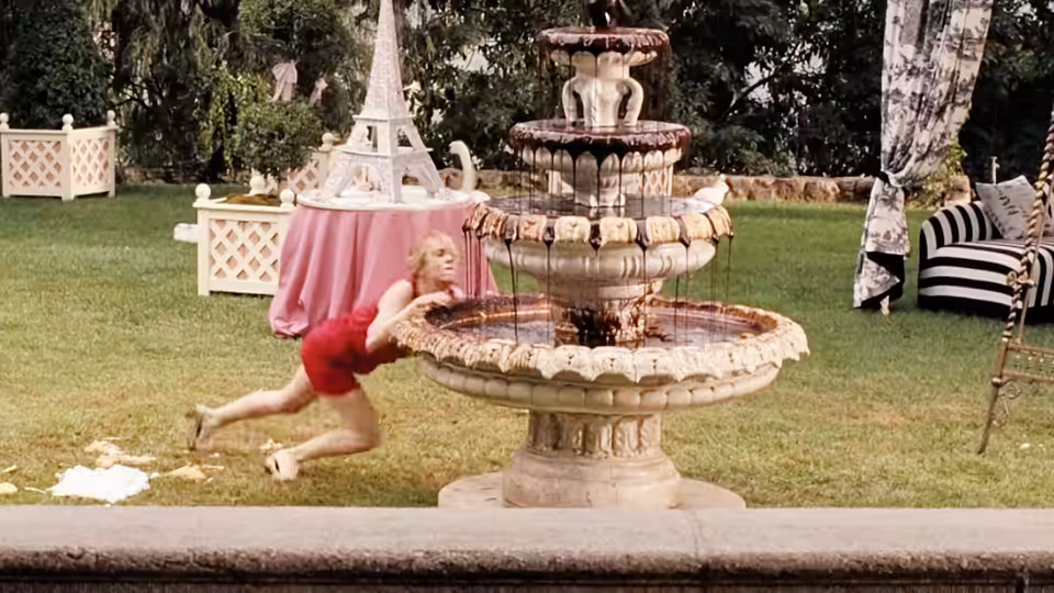 Annie (Kristen Wiig) in a red dress leaning over a garden fountain