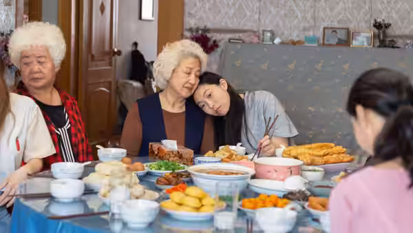 Billi (Awkwafina) rests her head on Nai Nai at the family meal