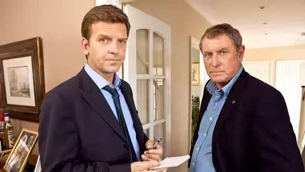 Tom Barnaby (John Nettles) indoors beside a colleague with a notebook
