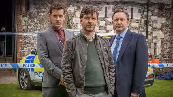 Three men standing in front of a police car by an old building