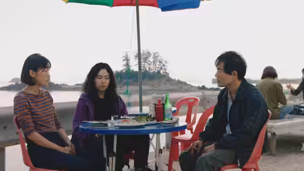 Freddie (Ji-min Park) joins a woman and a man at an outdoor table by the water