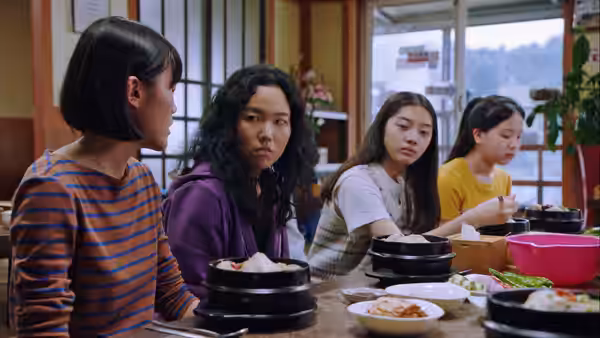 Freddie (Ji-min Park) sits with three young women at a table set with bowls of food
