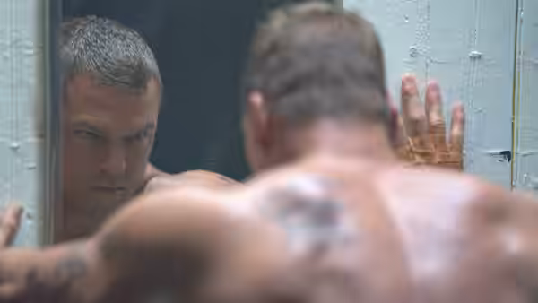 Shirtless muscular man with tattoos looking at his reflection in mirror