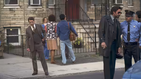 Man in gray suit standing on sidewalk near group and police officer