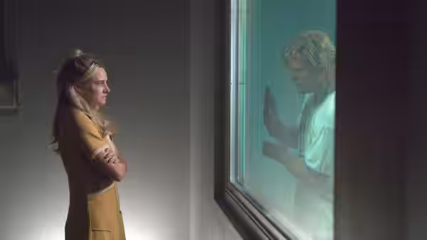 Woman with arms crossed facing man with hands pressed against glass window