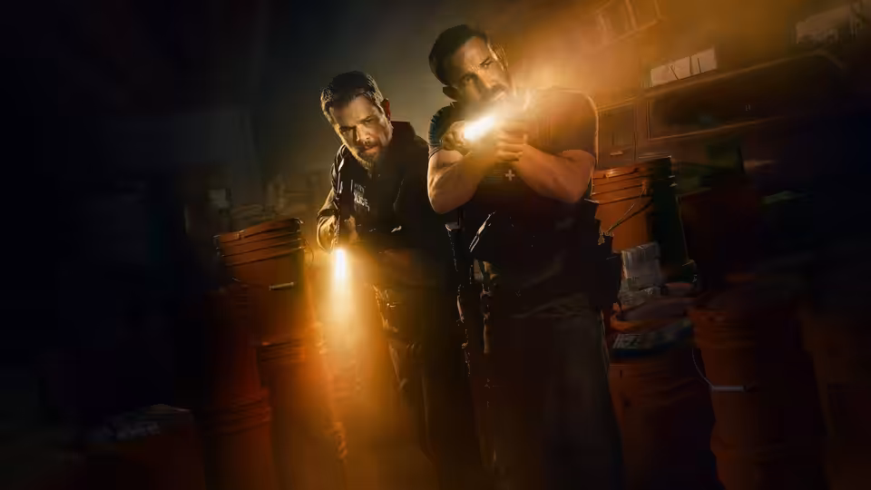 Matt Damon and Ben Affleck advancing through a dark warehouse with flashlights