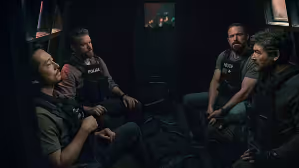 Four police officers seated inside a dimly lit vehicle or room