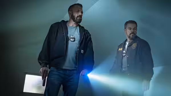 Ben Affleck and Kyle Chandler standing in a room lit by flashlights